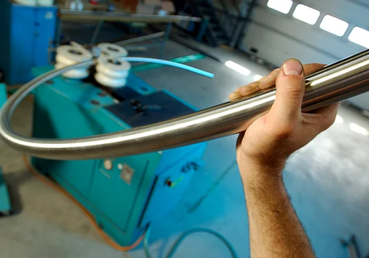 Eine Person hält ein gebogenes Metallrohr, umgeben von Maschinen und industrieller Ausrüstung. Eine Person hält ein gebogenes Metallrohr, umgeben von Maschinen und industrieller Ausrüstung.